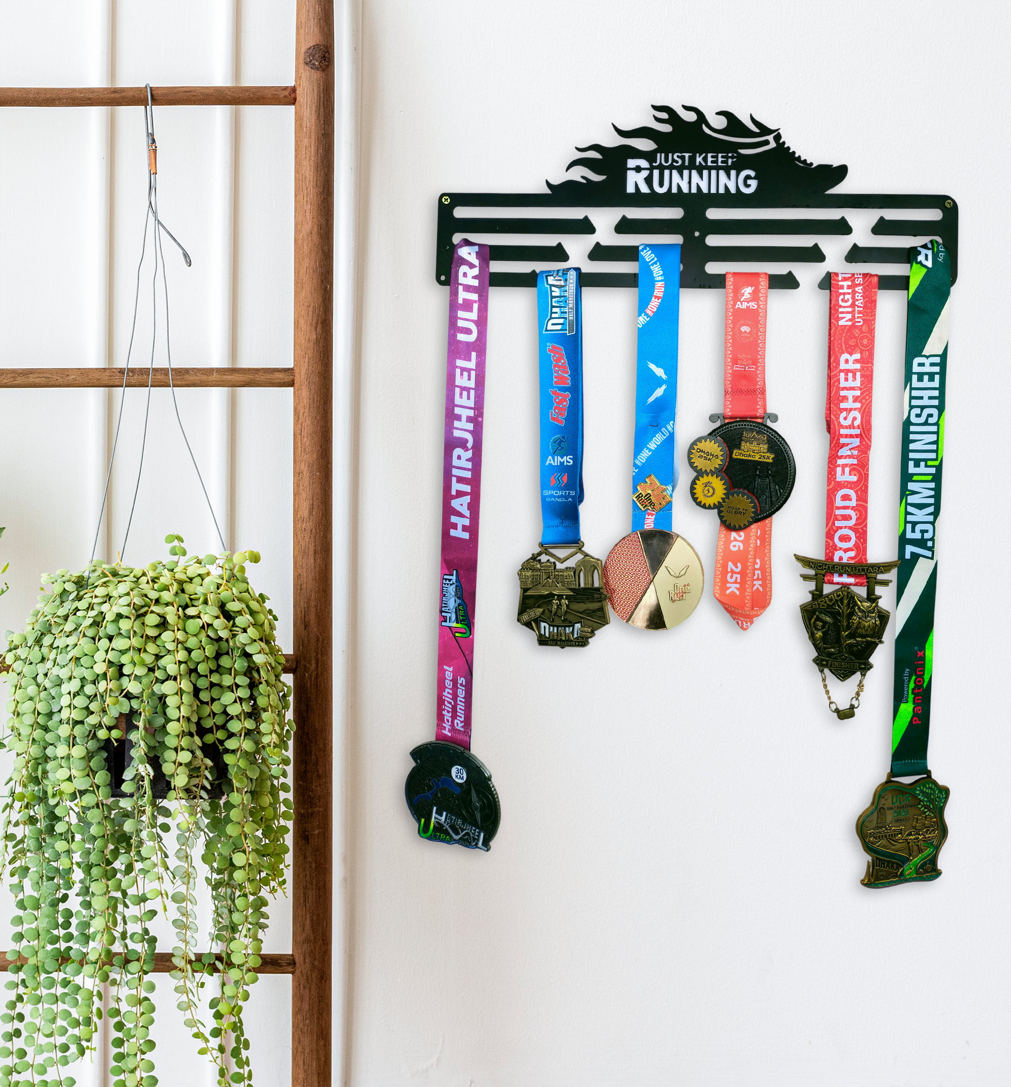 Black metal "Just Keep Running" medal display mounted on a white wall filled with colorful marathon finisher medals hanging from its bars.